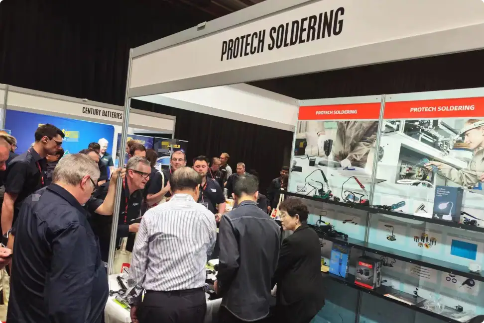Group of people attending a Protech Soldering booth at a trade show, exploring soldering equipment and technology displays.