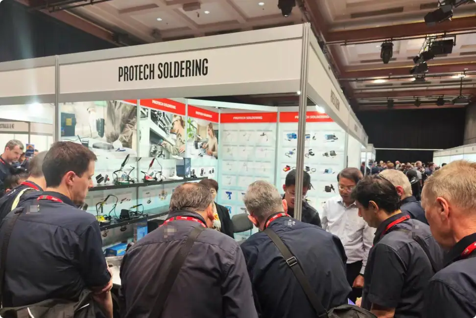 Attendees exploring Protech soldering solutions at a trade show booth with displays of soldering equipment and technical information.
