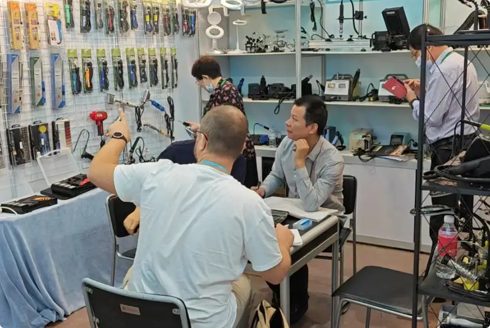 A group of customers and staff engaging in a discussion inside an electronics store, surrounded by various gadgets, tools, and electronic accessories displayed on shelves and tables.