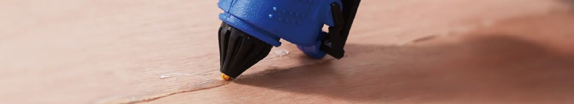 Hot glue gun applying adhesive to wood surface for craft project.