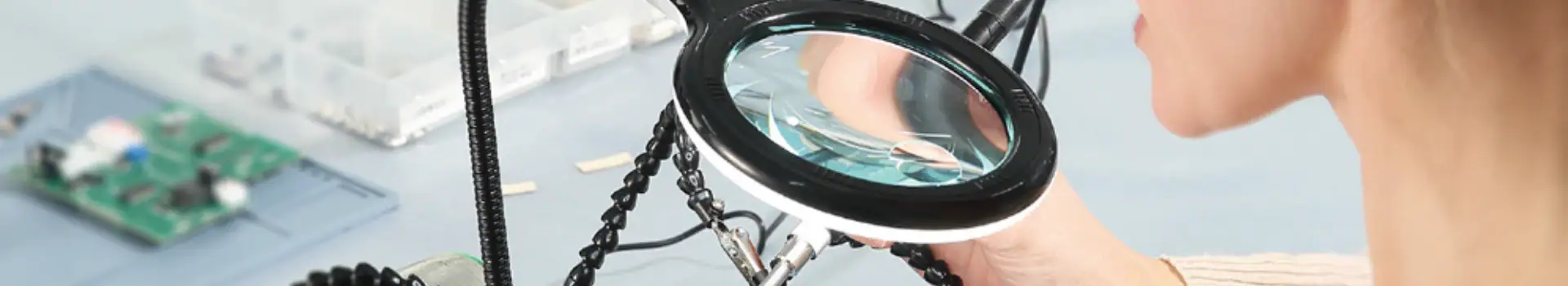 Technician examining a microchip with a magnifying glass during electronic component testing.
