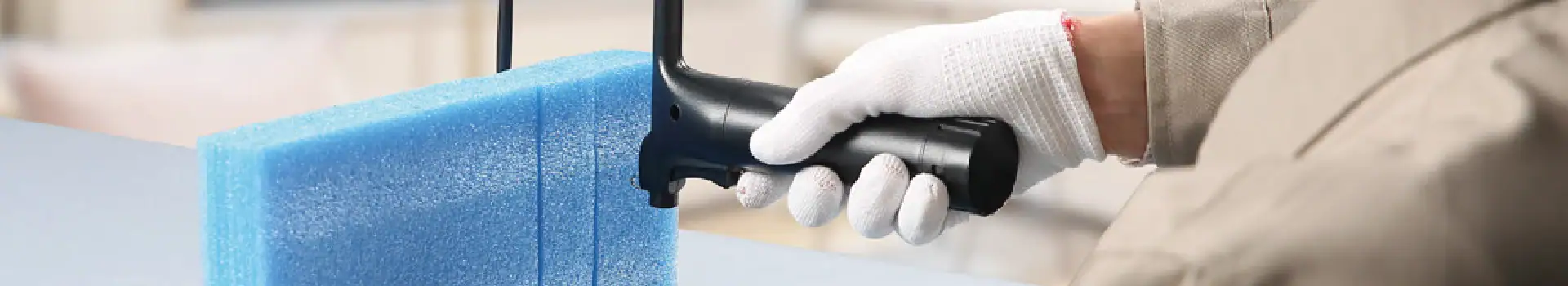 An operator wearing gloves uses a hot wire cutter to precisely shape blue foam material. This image highlights professional foam cutting techniques for manufacturing or crafting purposes.