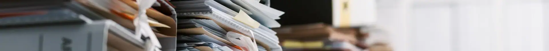 Office clutter with stacks of papers and files, showcasing disorganized workspace with documents, folders, and office supplies. Ideal for articles on organization, productivity, or office management.