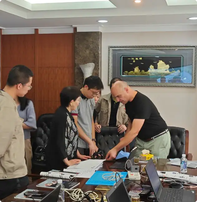 Collaborative team meeting in a professional office, with people discussing documents and working on laptops around a conference table.