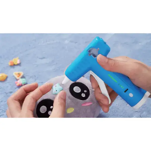 Adorable plush toy with large eyes and colorful accents, being personalized with a hot glue gun for a fun craft project.