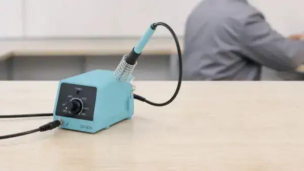 Close-up of an ESD-safe soldering workstation with a blue soldering station and a soldering iron, used for electronics repair and assembly.